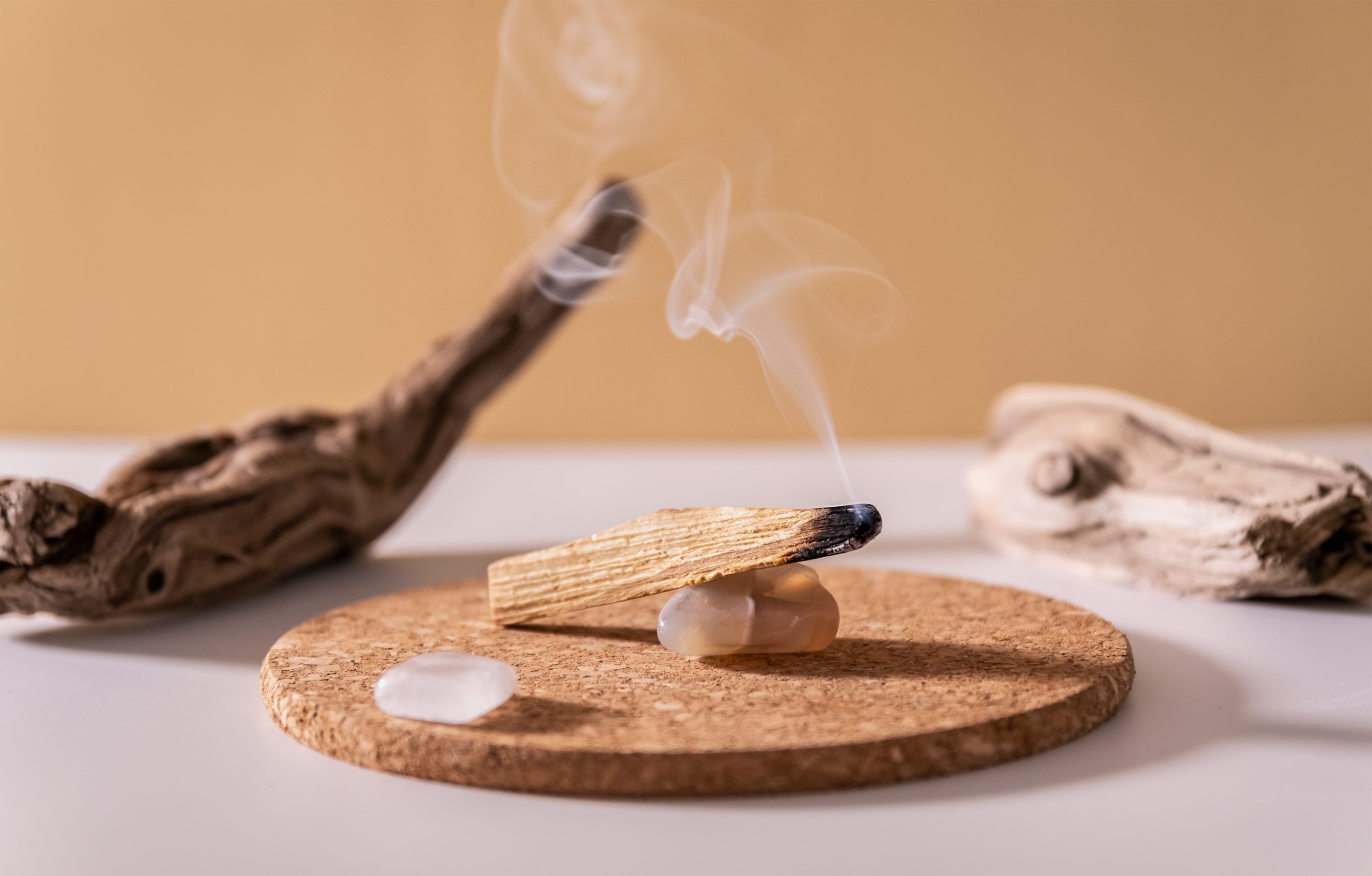 Rauchendes Palo-Santo-Holz auf rundem Korkuntersetzer mit Edelsteinen und Treibholz – beruhigendes Naturaroma für Ritual- und Raumduftanwendungen.“