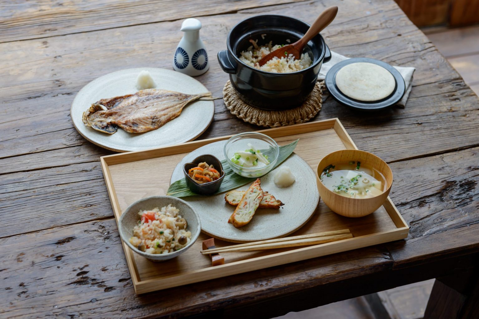 Traditionelles japanisches Frühstücks-Set mit gegrilltem Fisch, Misosuppe, Reis aus dem Donabe-Topf und frischem Gemüse – die perfekte Inspiration für ein eigenes vegetarisches Donabe-Rezept, serviert auf einem rustikalen Holztisch.