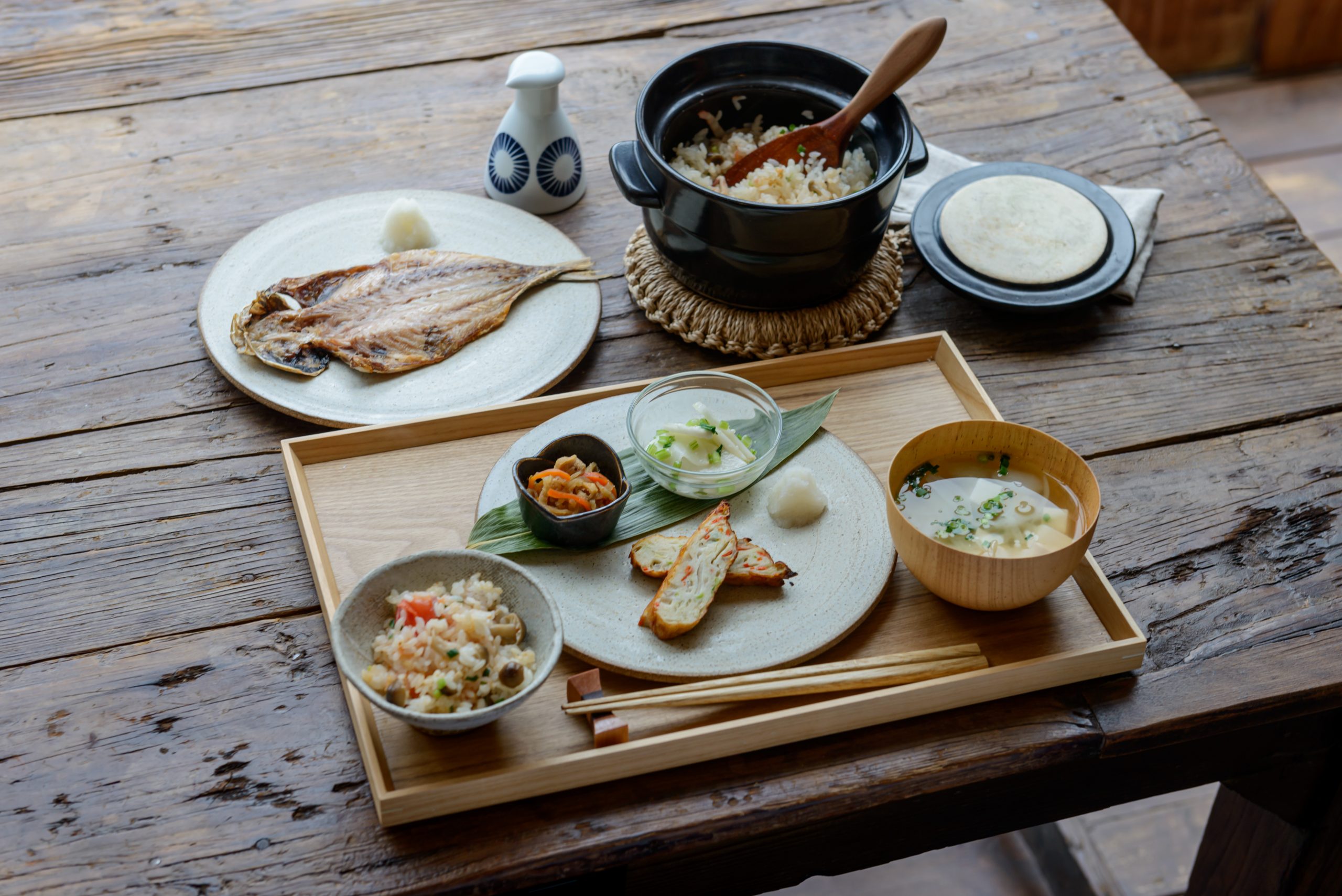 Traditionelles japanisches Frühstücks-Set mit gegrilltem Fisch, Misosuppe, Reis aus dem Donabe-Topf und frischem Gemüse – die perfekte Inspiration für ein eigenes vegetarisches Donabe-Rezept, serviert auf einem rustikalen Holztisch.
