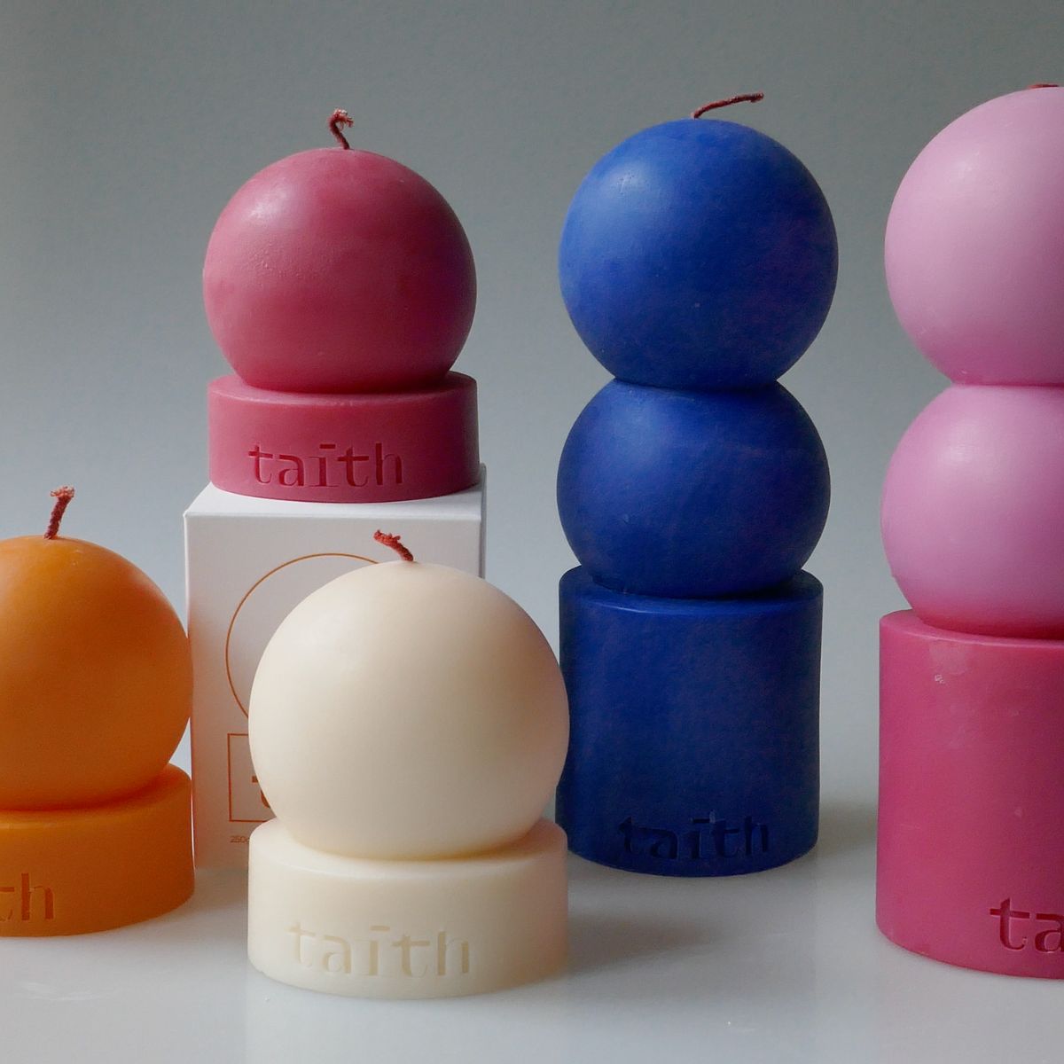 Bougies design colorées de Taith, de formes sphériques modernes, rouges, bleues, roses, blanches et oranges, présentées comme des bougies parfumées décoratives.