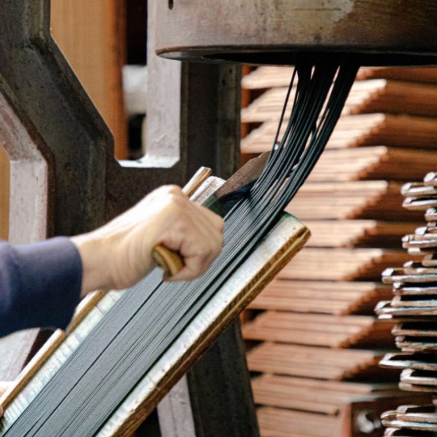 Handarbeit bei der Herstellung von Räucherstäbchen: Eine Person formt und glättet feine Stäbchenstränge an einer traditionellen Maschine – kunstvolle Produktion natürlicher Räucherwaren.Maschine – Manufakturarbeit für hochwertige Produkte.