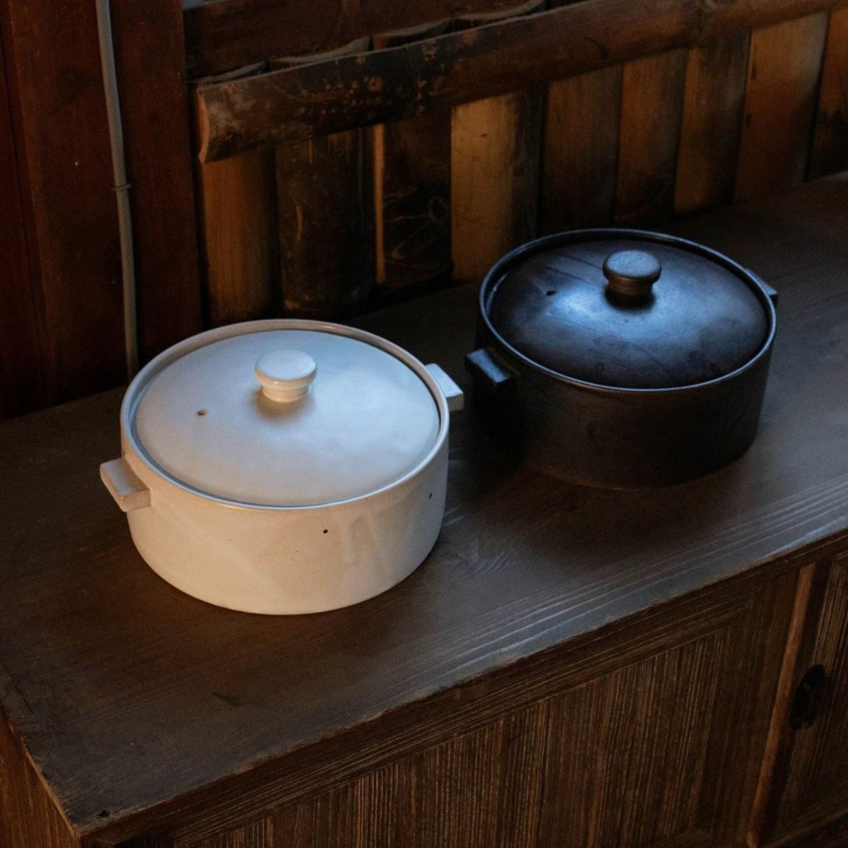 Japacolle Donabe – zwei japanische Keramik-Kochtöpfe in Weiß und Schwarz, nebeneinander auf Holzoberfläche präsentiert.