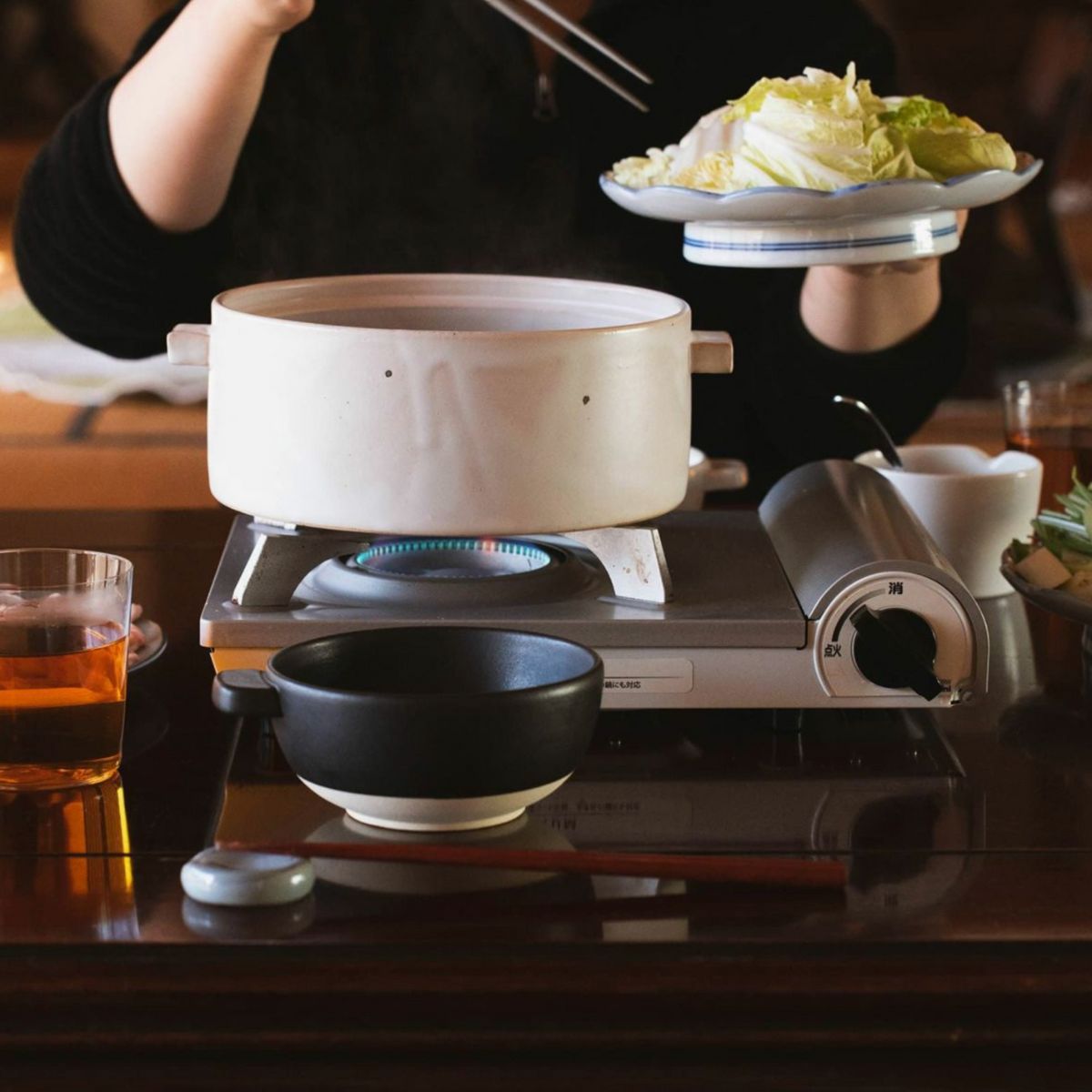Japacolle Donabe – white Japanese ceramic pot on a gas stove, fresh vegetables are added using chopsticks.