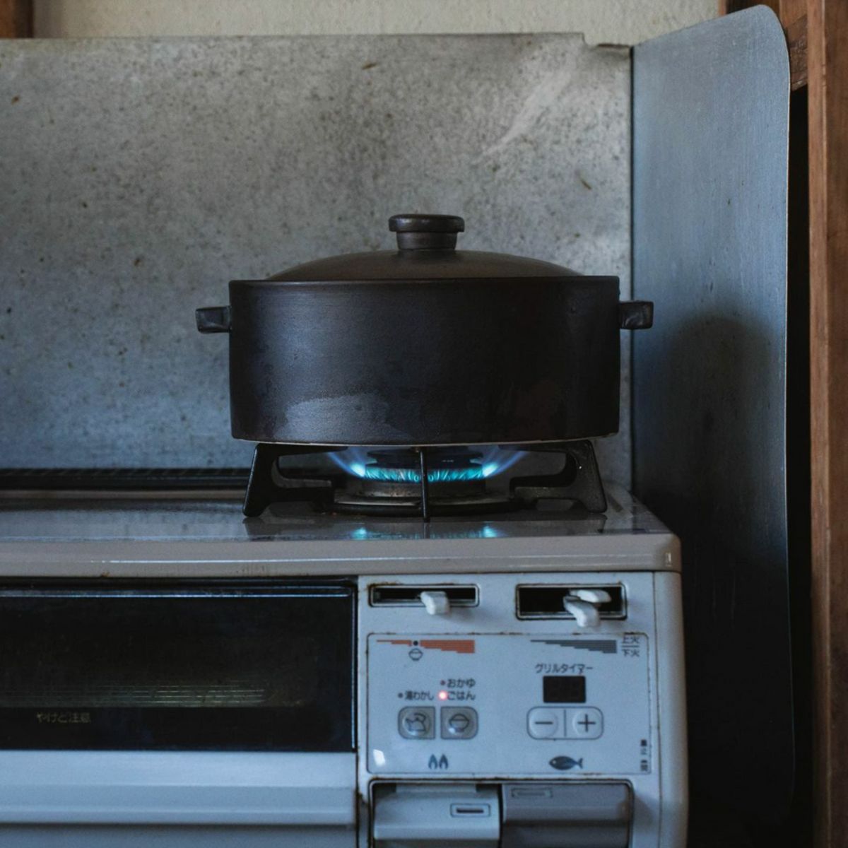 Japacolle Donabe – black Japanese ceramic rice cooking pot on gas stove with open flame, traditional cooking.