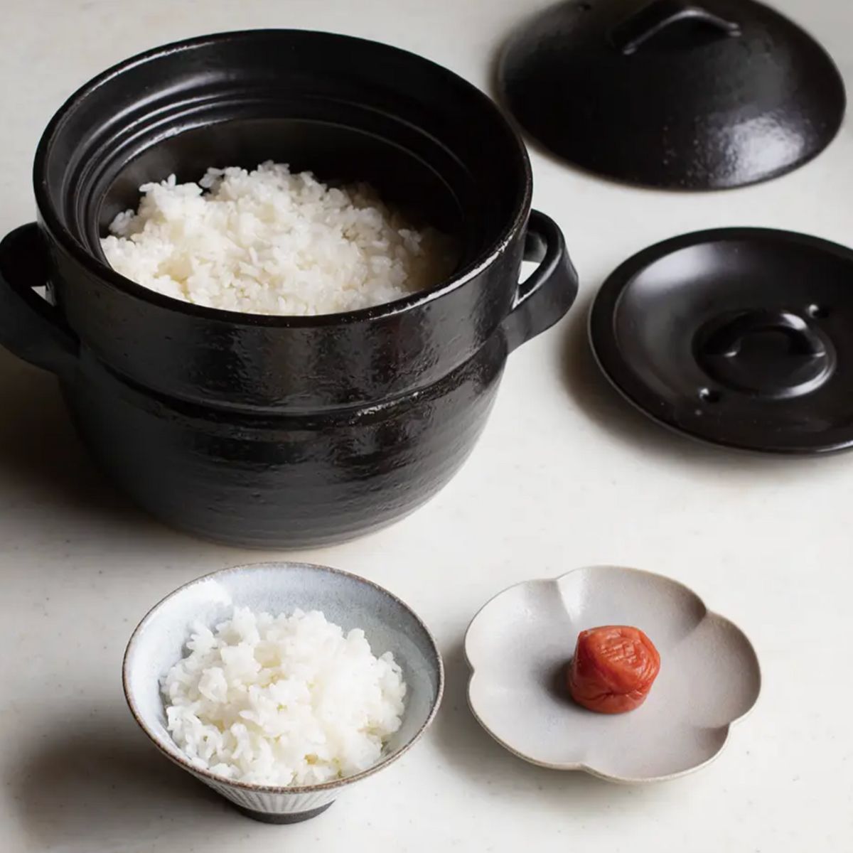 Japacolle Donabe – schwarzer japanischer Keramik-Reiskochtopf mit frisch gekochtem Reis, serviert in traditionellen Schalen.