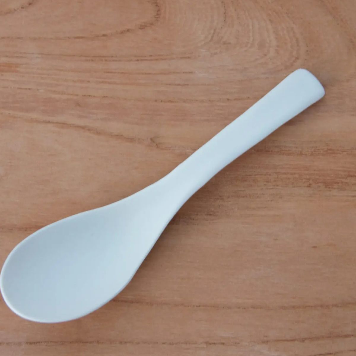 Design Löffel von Kamoshika. Japanischer Küchenlöffel aus Keramik auf Holzoberfläche – minimalistisches Design in Weiß