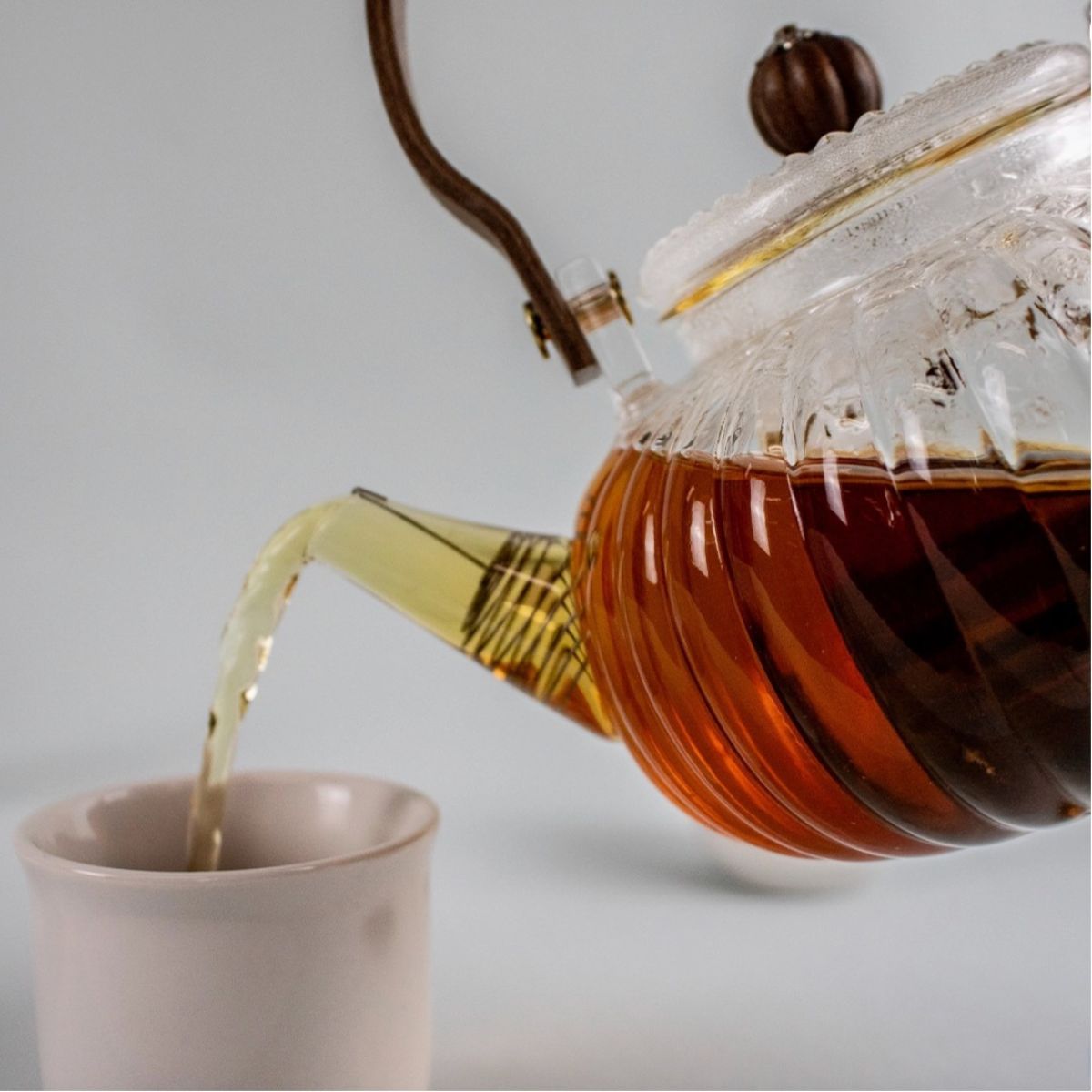 Una tetera de vidrio con mango de madera vierte té recién hecho en una taza blanca minimalista: un elegante ritual del té con un servicio de té de alta calidad.