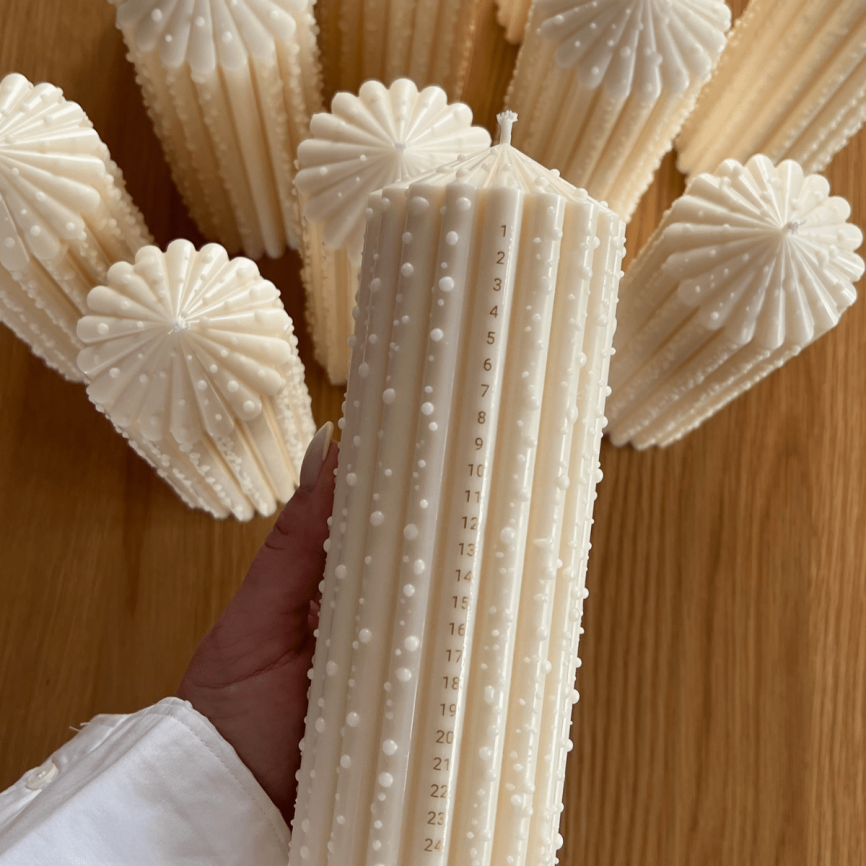 cremefarbene Studio M Candles Adventskerze mit 1–24 Datumsskala und erhabenen Wachspunkten, umgeben von weiteren identischen Kerzen